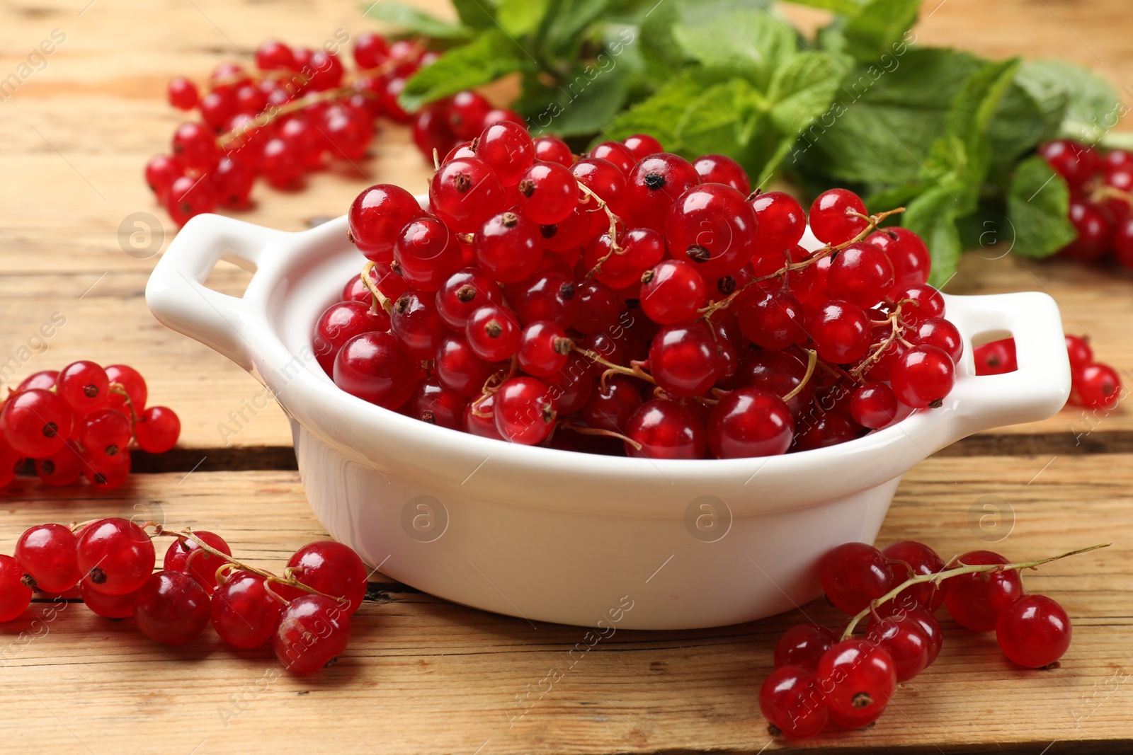 Photo of Fresh red currants in bowl and mint on wooden table, closeup