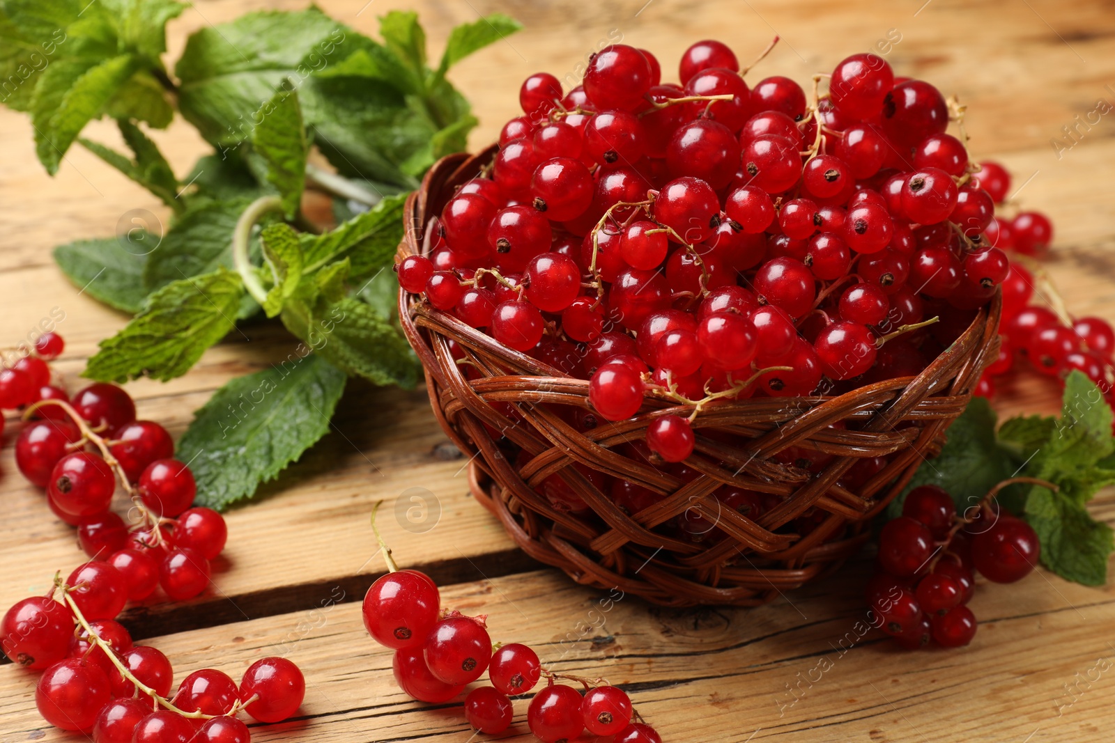 Photo of Fresh red currants in basket and mint on wooden table, closeup