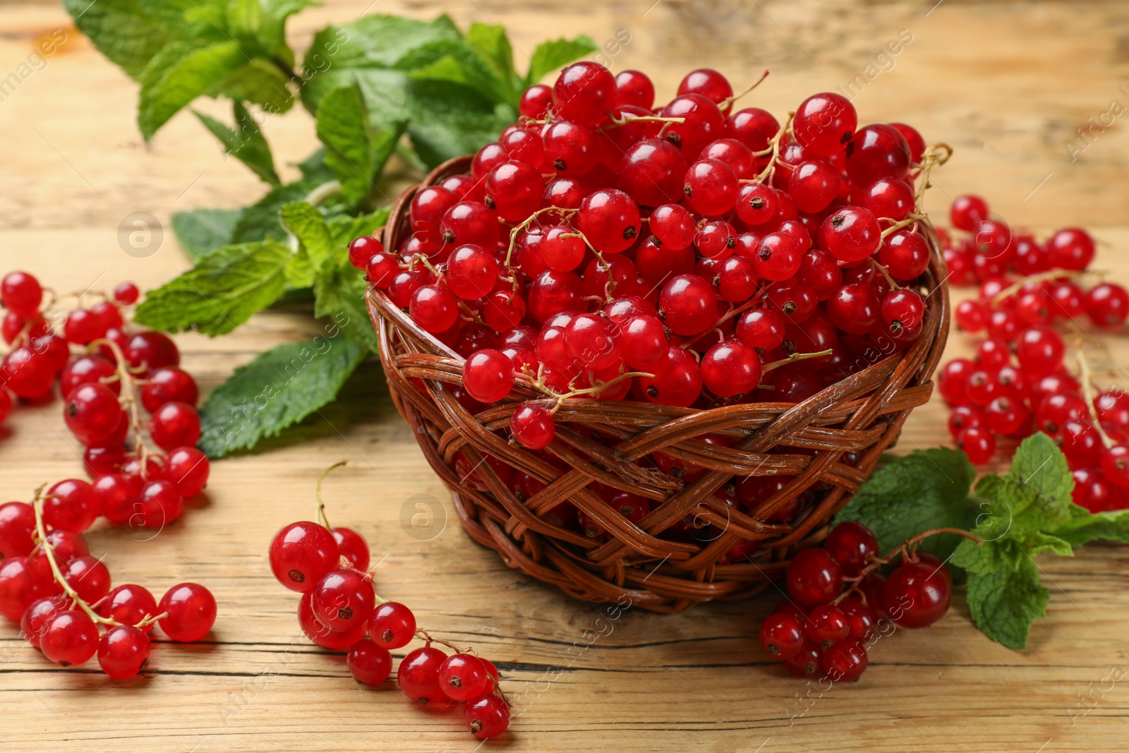 Photo of Fresh red currants in basket and mint on wooden table, closeup