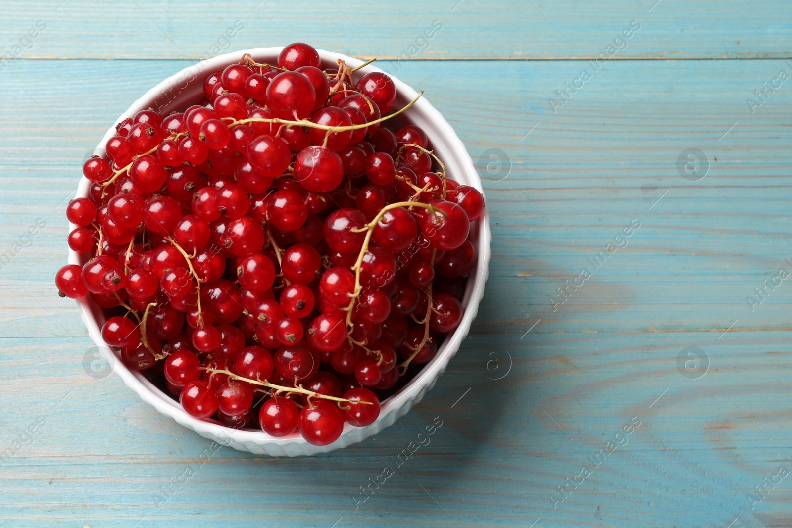 Photo of Fresh red currants in bowl on light blue wooden table, top view. Space for text