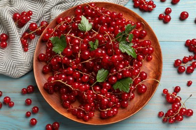 Photo of Fresh red currants and leaves on light blue wooden table, flat lay