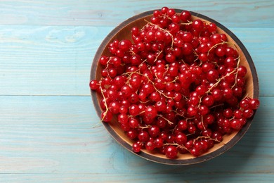 Photo of Fresh red currants in bowl on light blue wooden table, top view. Space for text