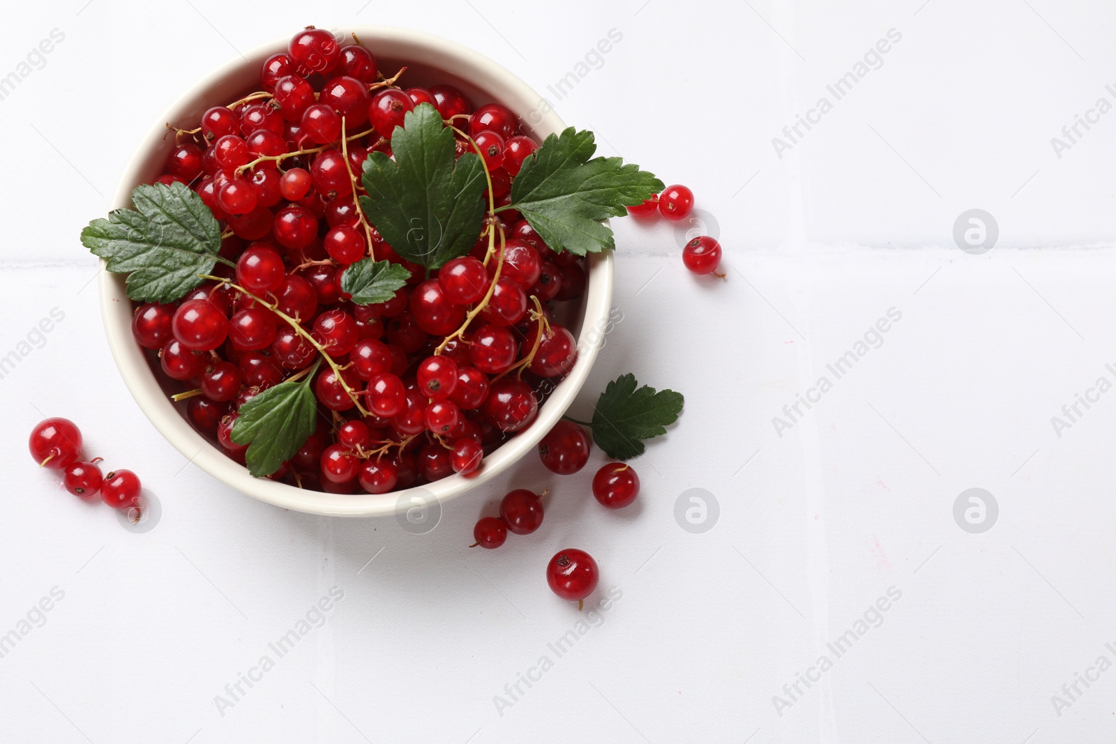 Photo of Fresh red currants and leaves in bowl on white table, top view