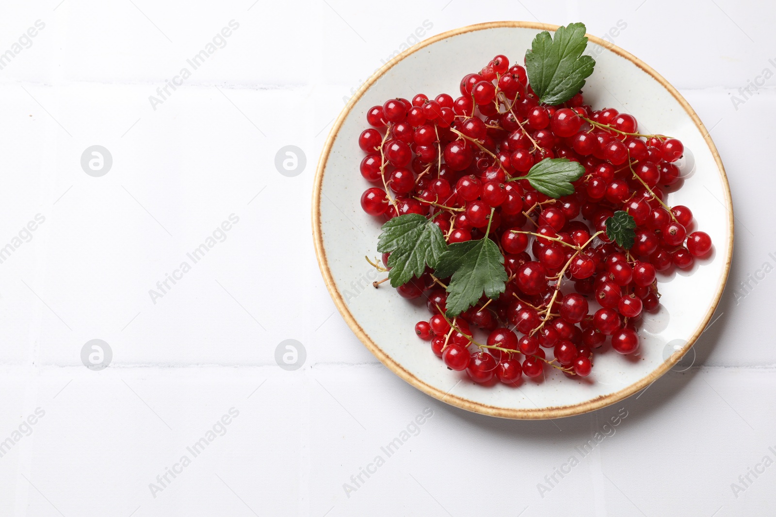 Photo of Fresh red currants and green leaves on white table, top view. Space for text