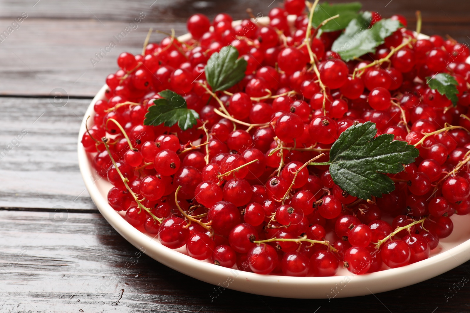 Photo of Fresh red currants and green leaves on wooden table, closeup