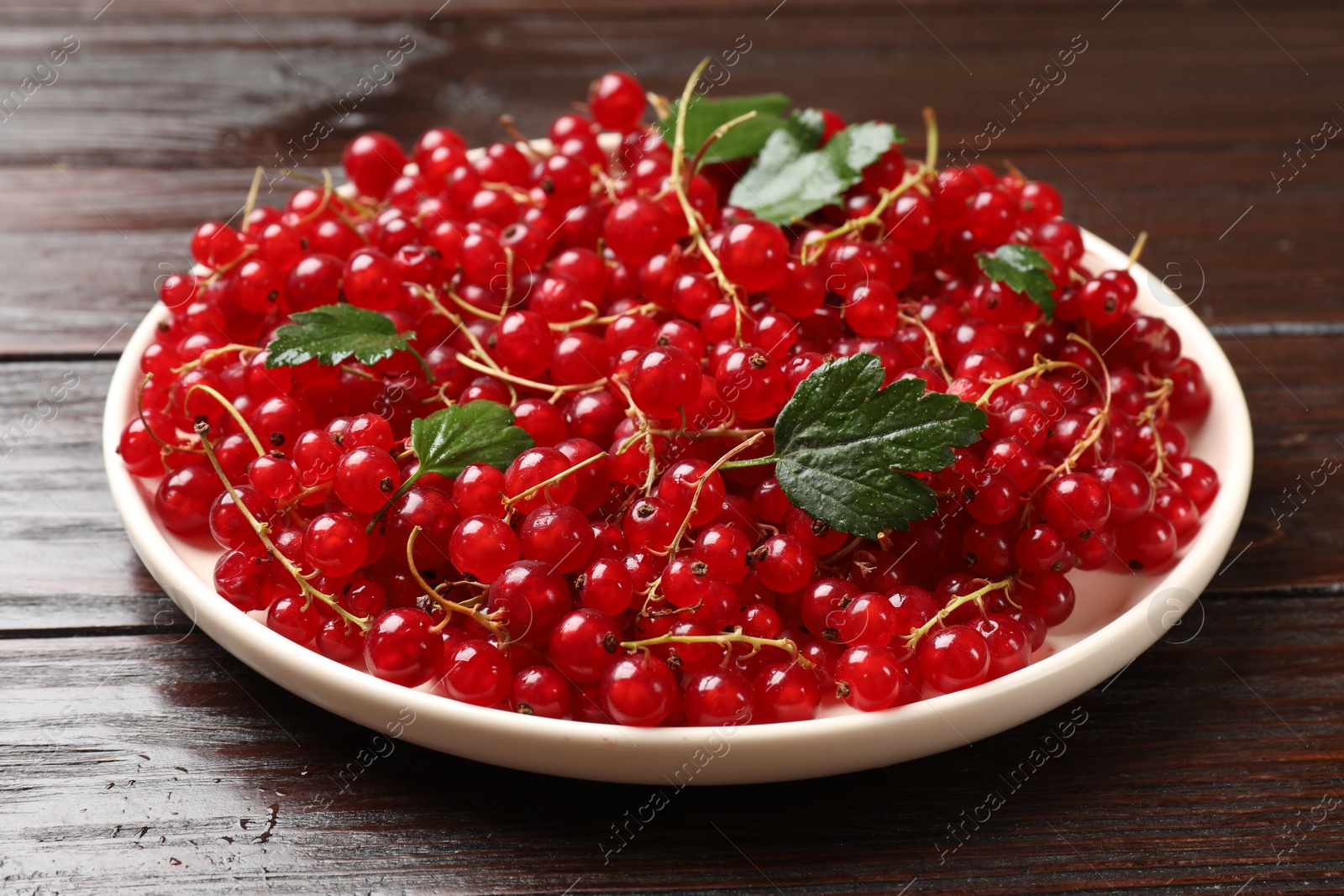 Photo of Fresh red currants and green leaves on wooden table, closeup