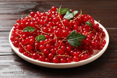 Photo of Fresh red currants and green leaves on wooden table, closeup