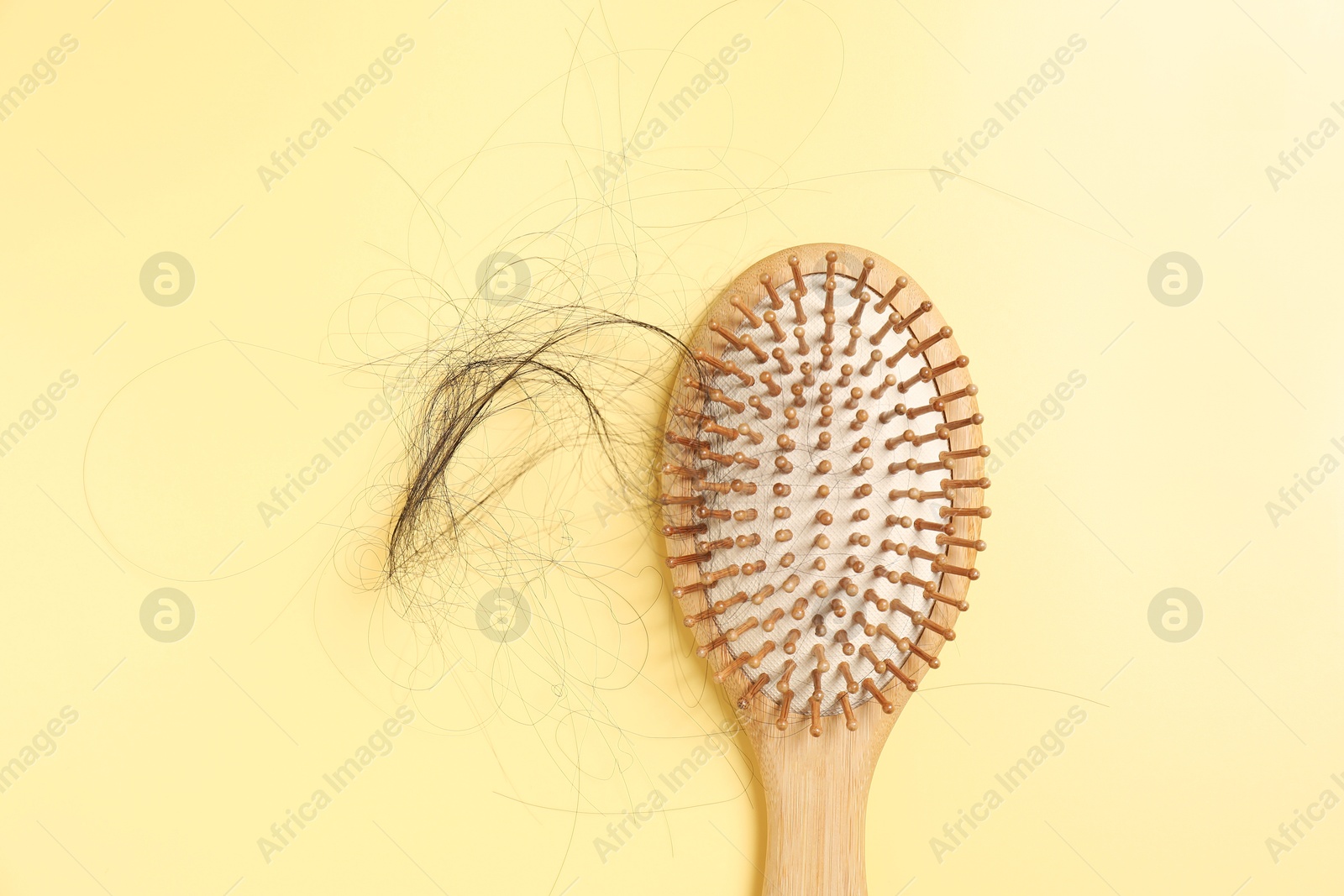 Photo of Wooden brush with lost hair on yellow background, top view