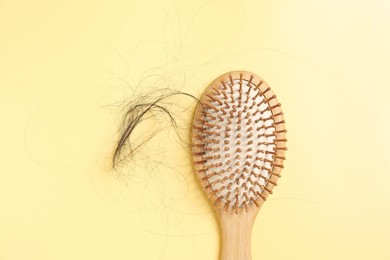 Wooden brush with lost hair on yellow background, top view