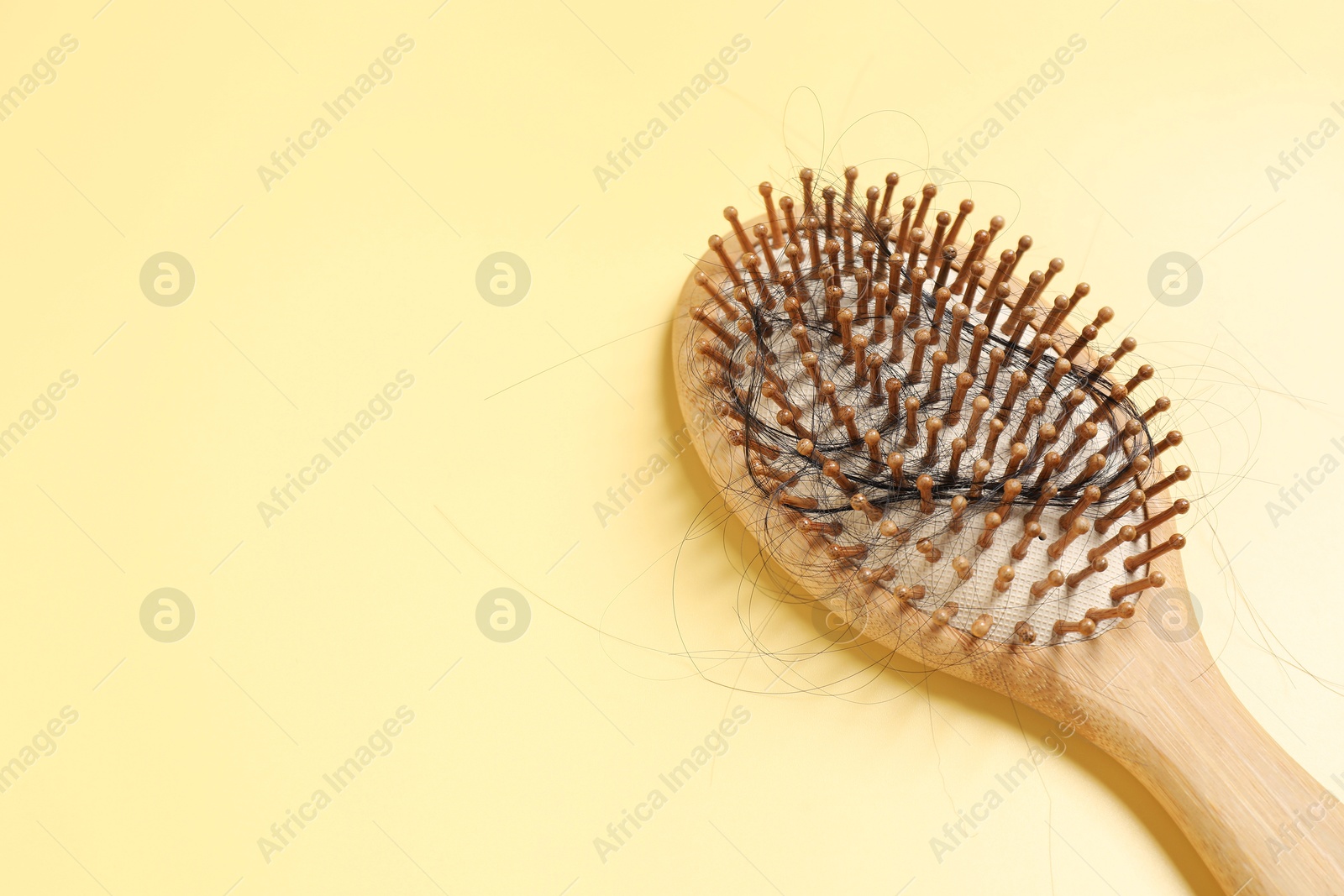 Photo of Wooden brush with lost hair on yellow background, space for text