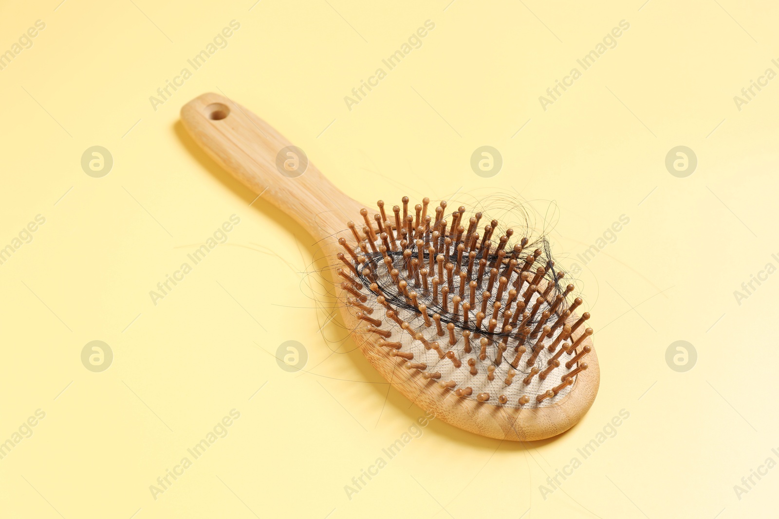 Photo of Wooden brush with lost hair on yellow background