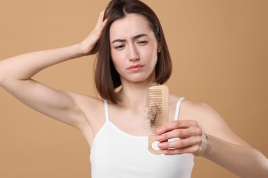 Photo of Stressed woman holding comb with lost hair on light brown background, selective focus. Alopecia problem