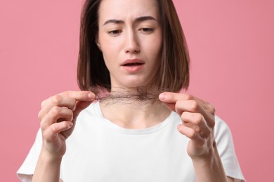 Photo of Sad woman holding clump of lost hair on pink background, selective focus. Alopecia problem