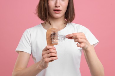 Photo of Woman taking her lost hair from comb on pink background, closeup. Alopecia problem