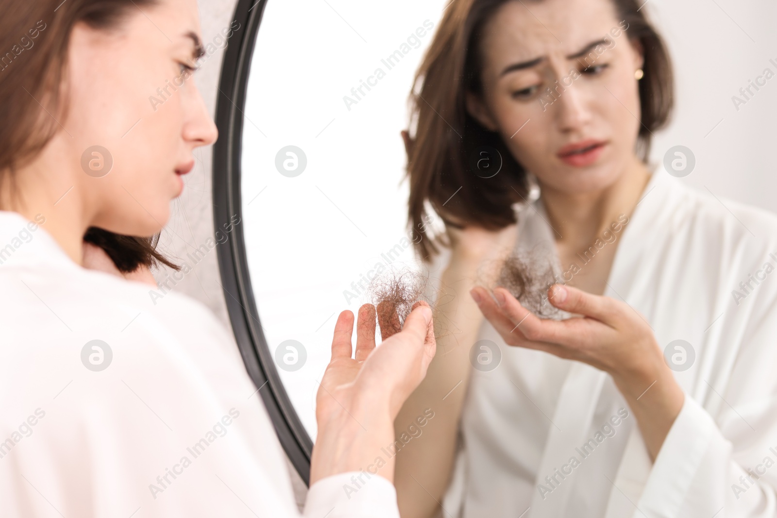 Photo of Sad woman holding clump of lost hair near mirror indoors. Alopecia problem