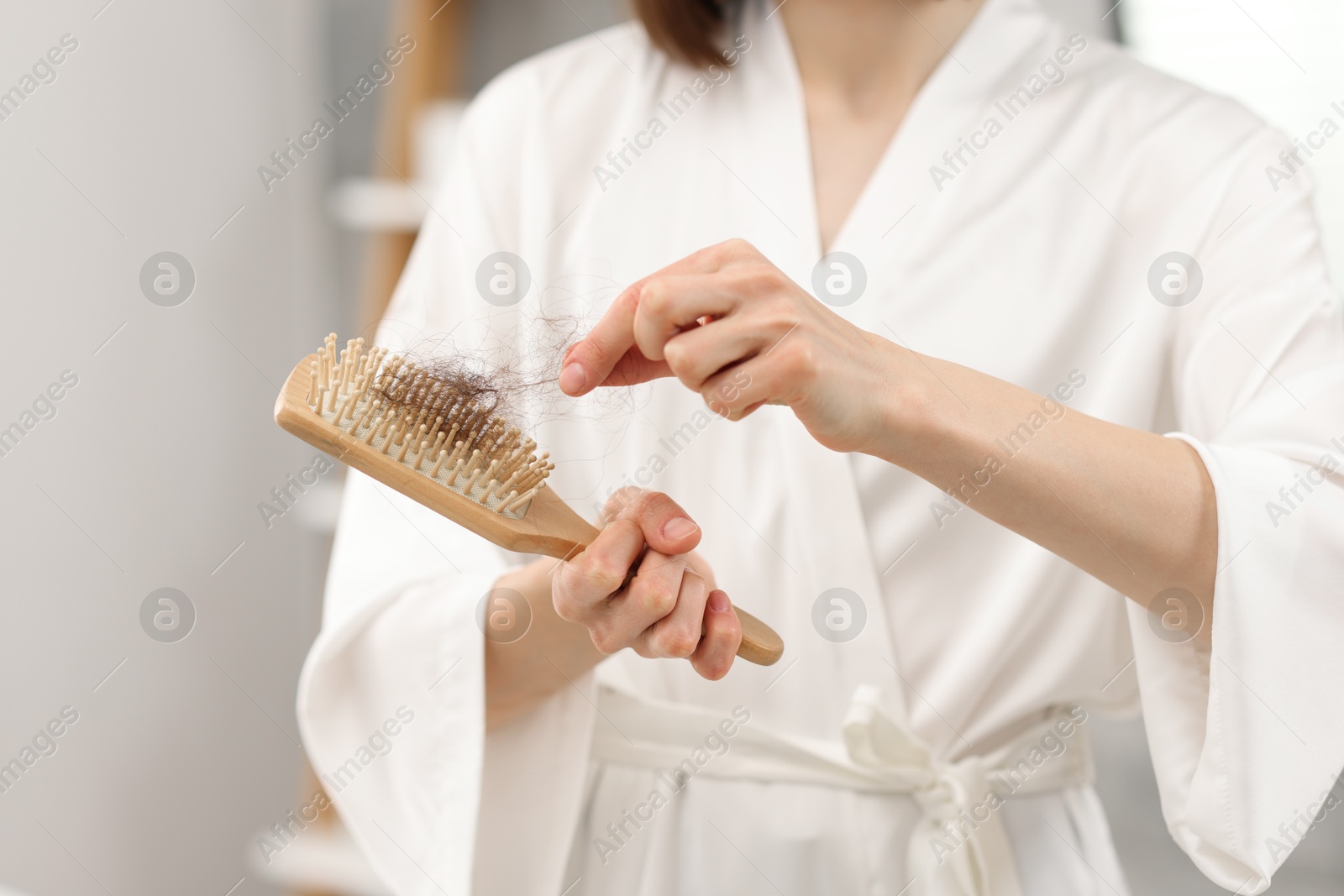 Photo of Woman taking her lost hair from brush at home, closeup. Alopecia problem