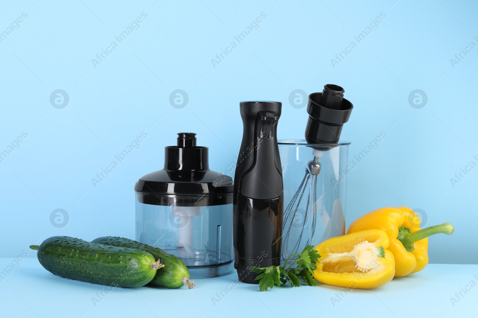 Photo of Hand blender kit and fresh vegetables on light blue background