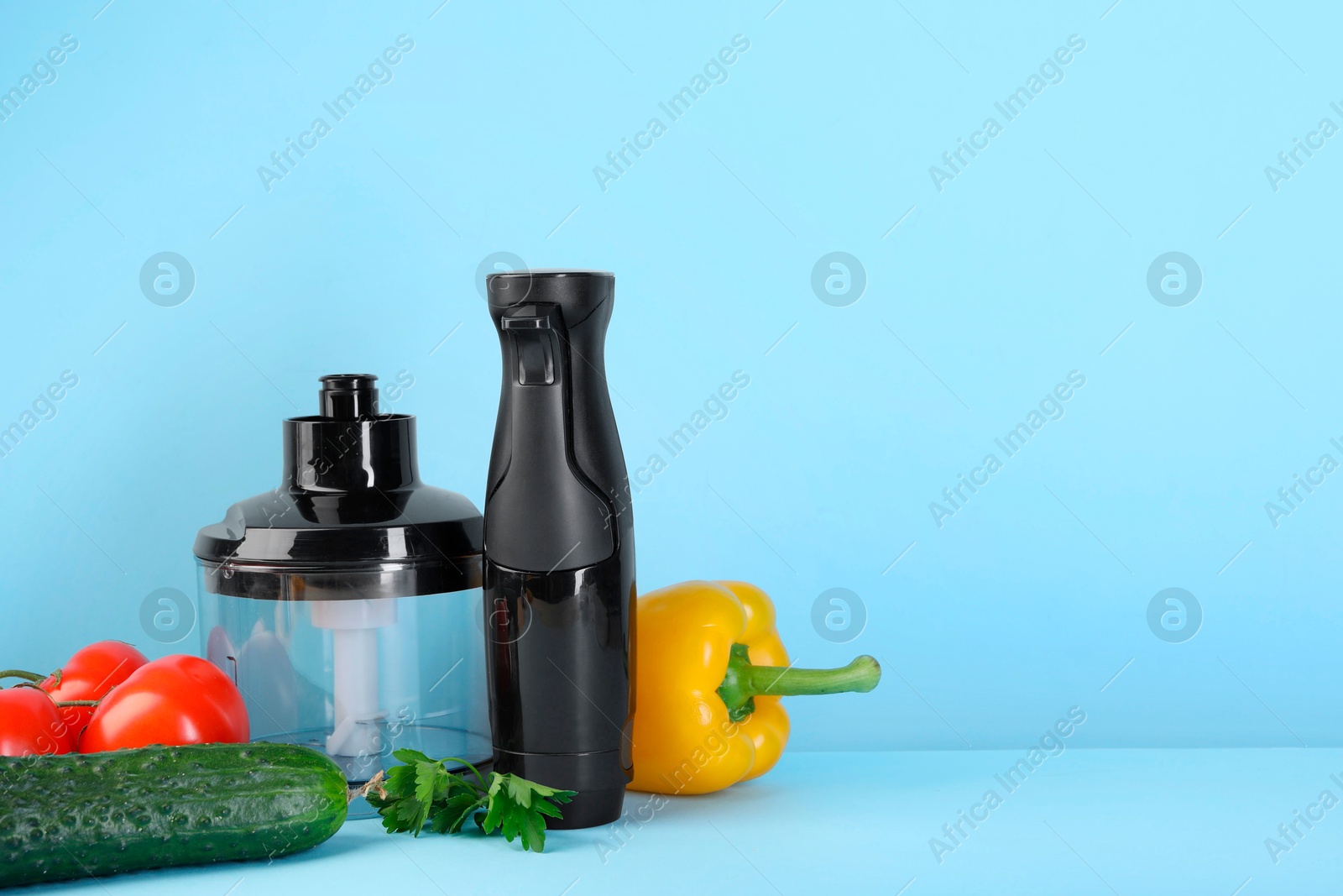 Photo of Hand blender kit, fresh vegetables and parsley on light blue background, space for text