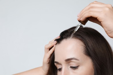 Photo of Hair loss problem. Woman applying serum onto hairline on light background, closeup. Space for text