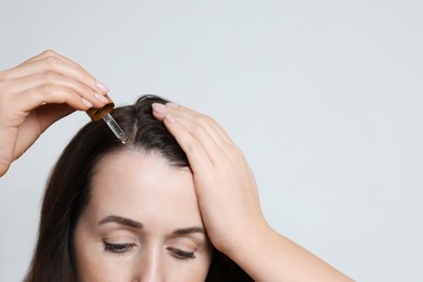 Photo of Hair loss problem. Woman applying serum onto hairline on light background, closeup. Space for text