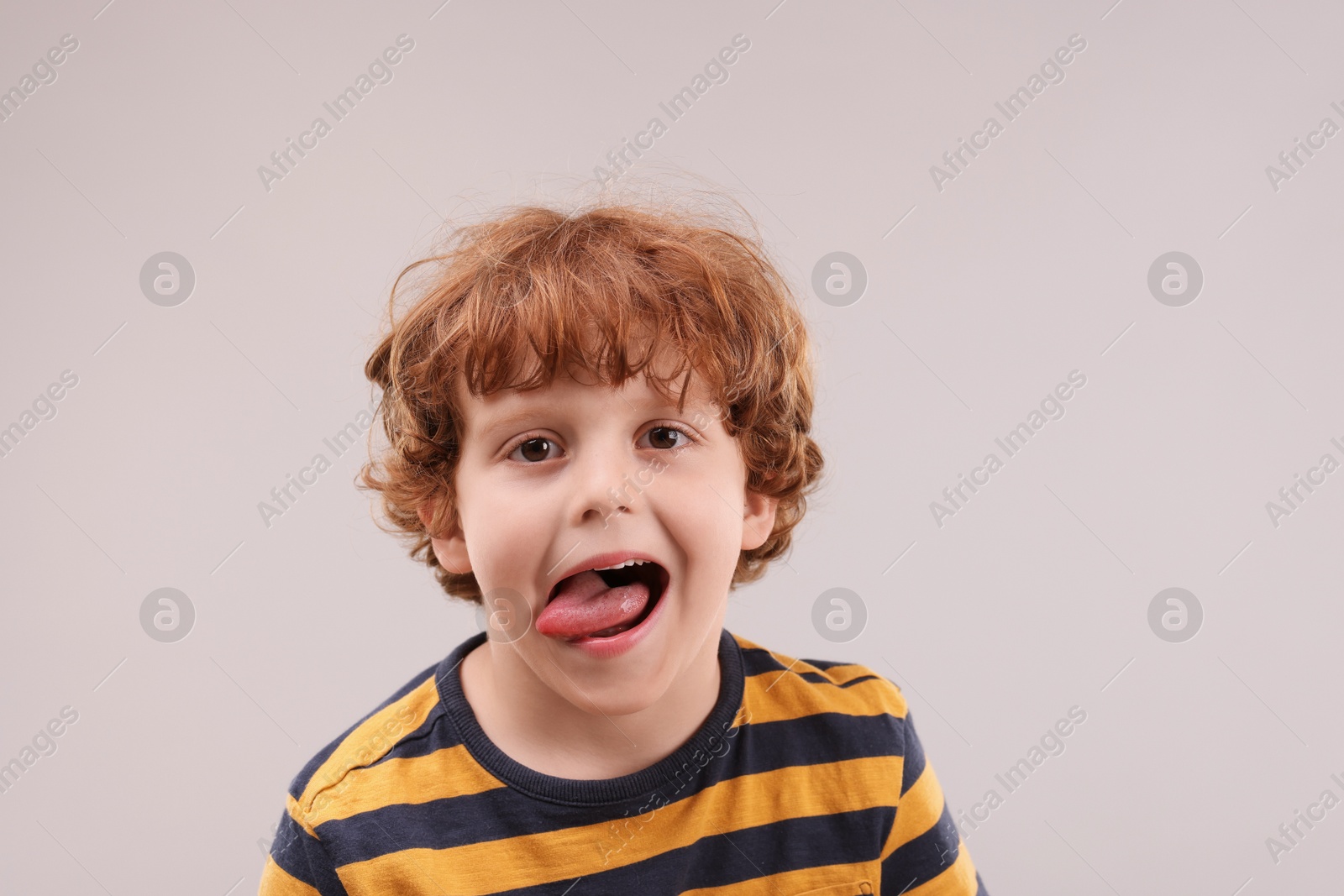 Photo of Portrait of emotional little boy showing tongue on grey background