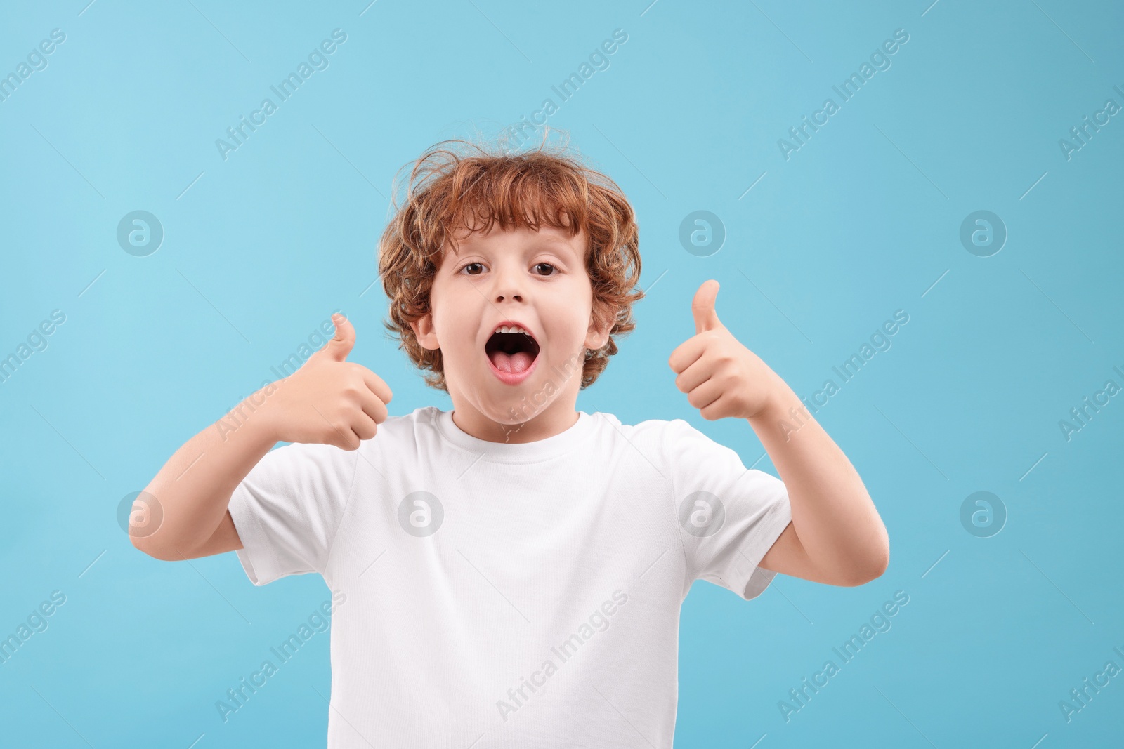 Photo of Portrait of emotional little boy showing thumbs up on light blue background