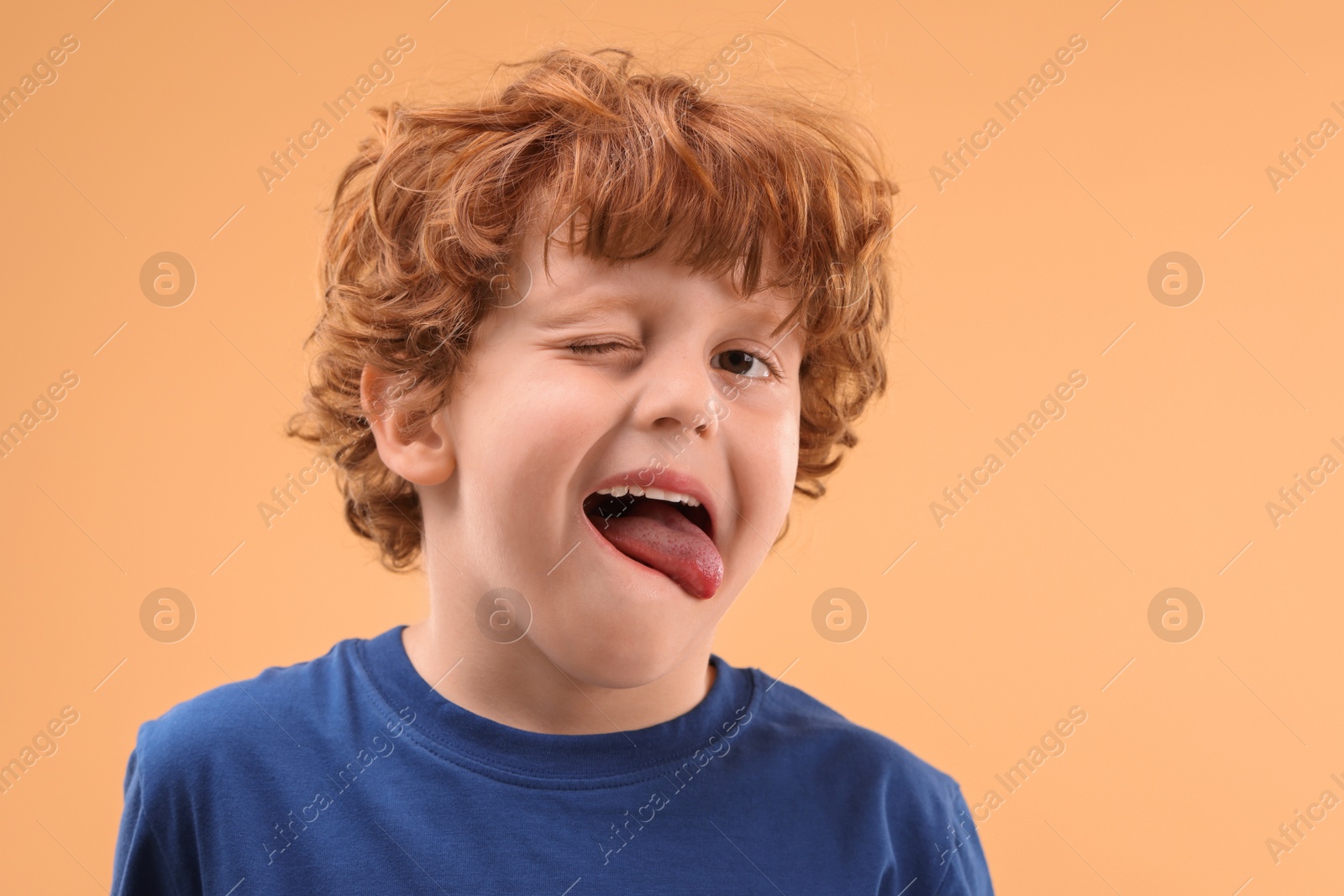 Photo of Portrait of cute little boy showing tongue on beige background