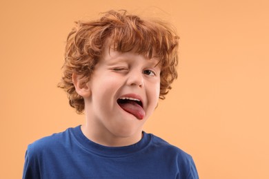 Photo of Portrait of cute little boy showing tongue on beige background