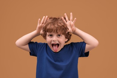 Photo of Portrait of cute little boy showing tongue on beige background