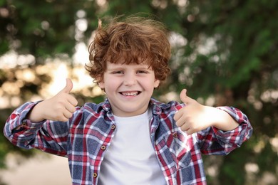 Photo of Portrait of cute little boy showing thumbs up outdoors