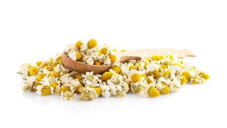 Pile of chamomile flowers and wooden spoon isolated on white