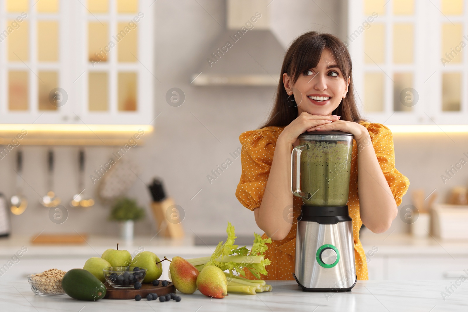 Photo of Young woman making delicious smoothie with blender at white marble table in kitchen