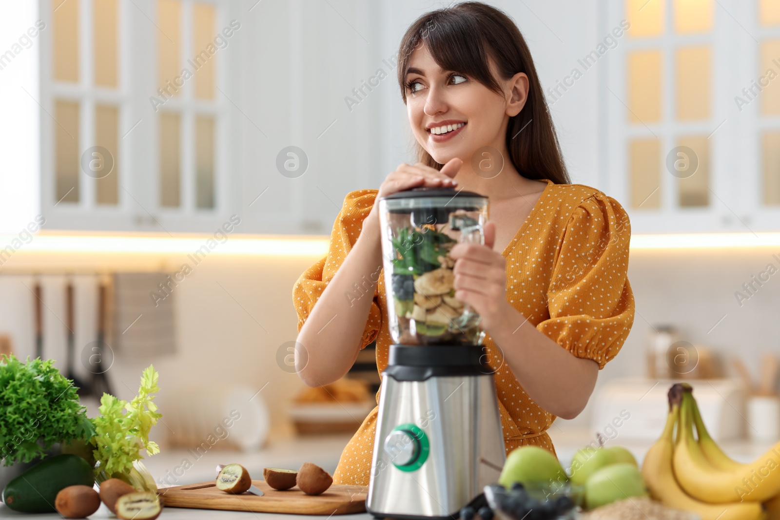 Photo of Young woman making delicious smoothie with blender at white marble table in kitchen