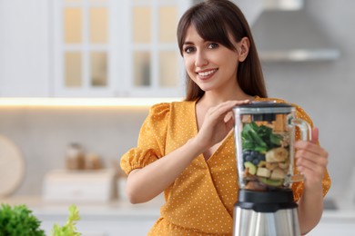 Photo of Young woman making delicious smoothie with blender in kitchen. Space for text
