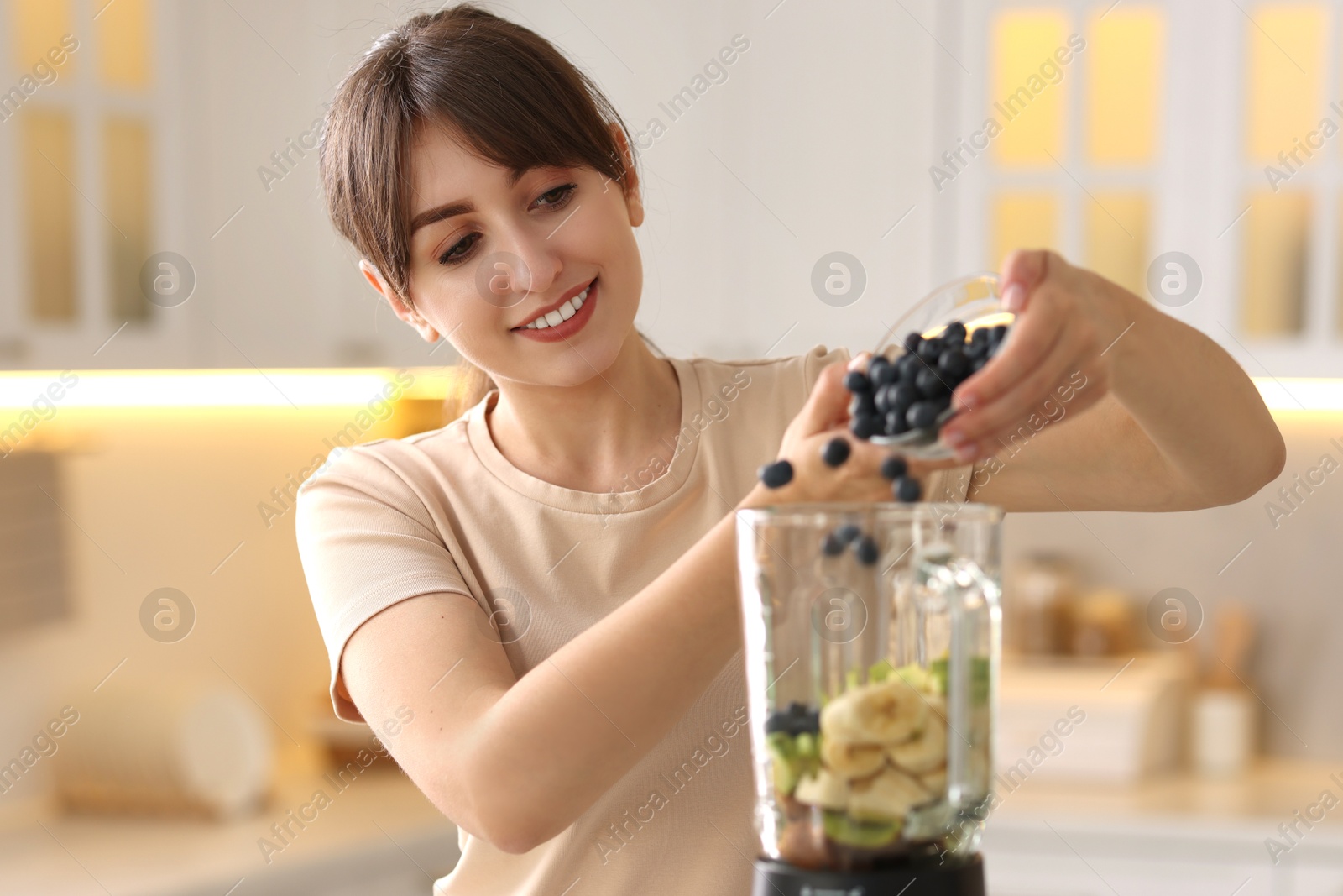 Photo of Young woman making delicious smoothie with blender in kitchen