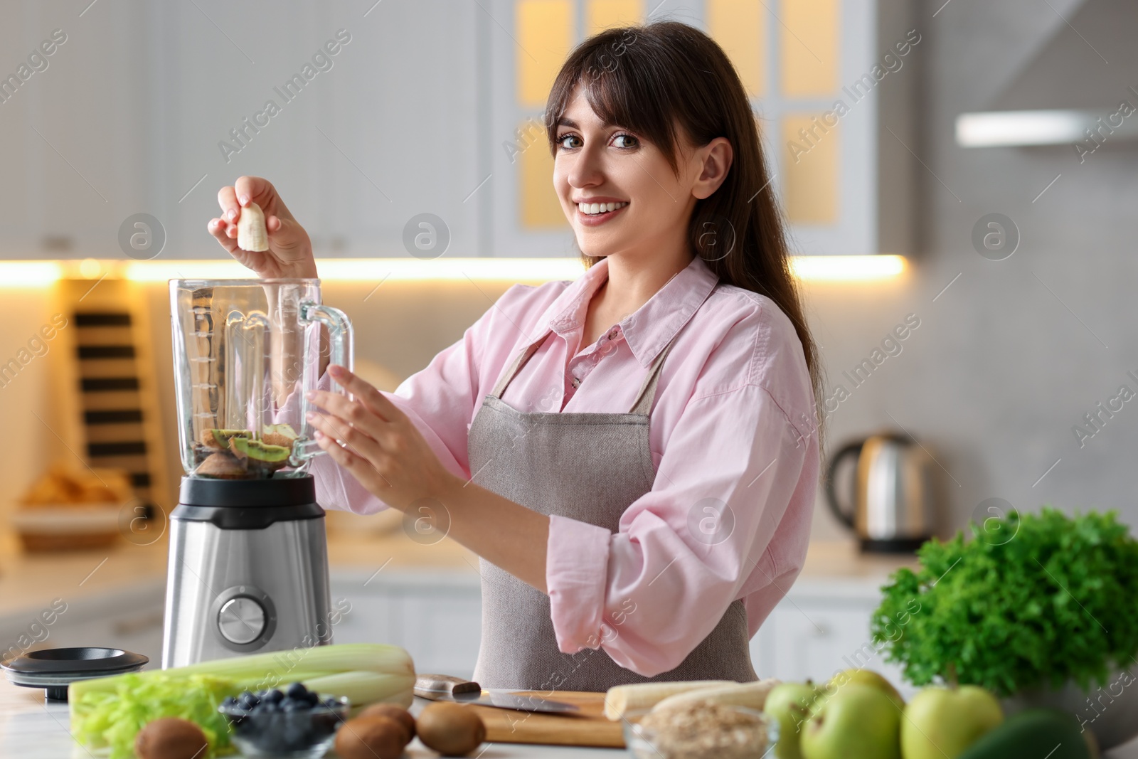 Photo of Young woman making delicious smoothie with blender at white marble table in kitchen