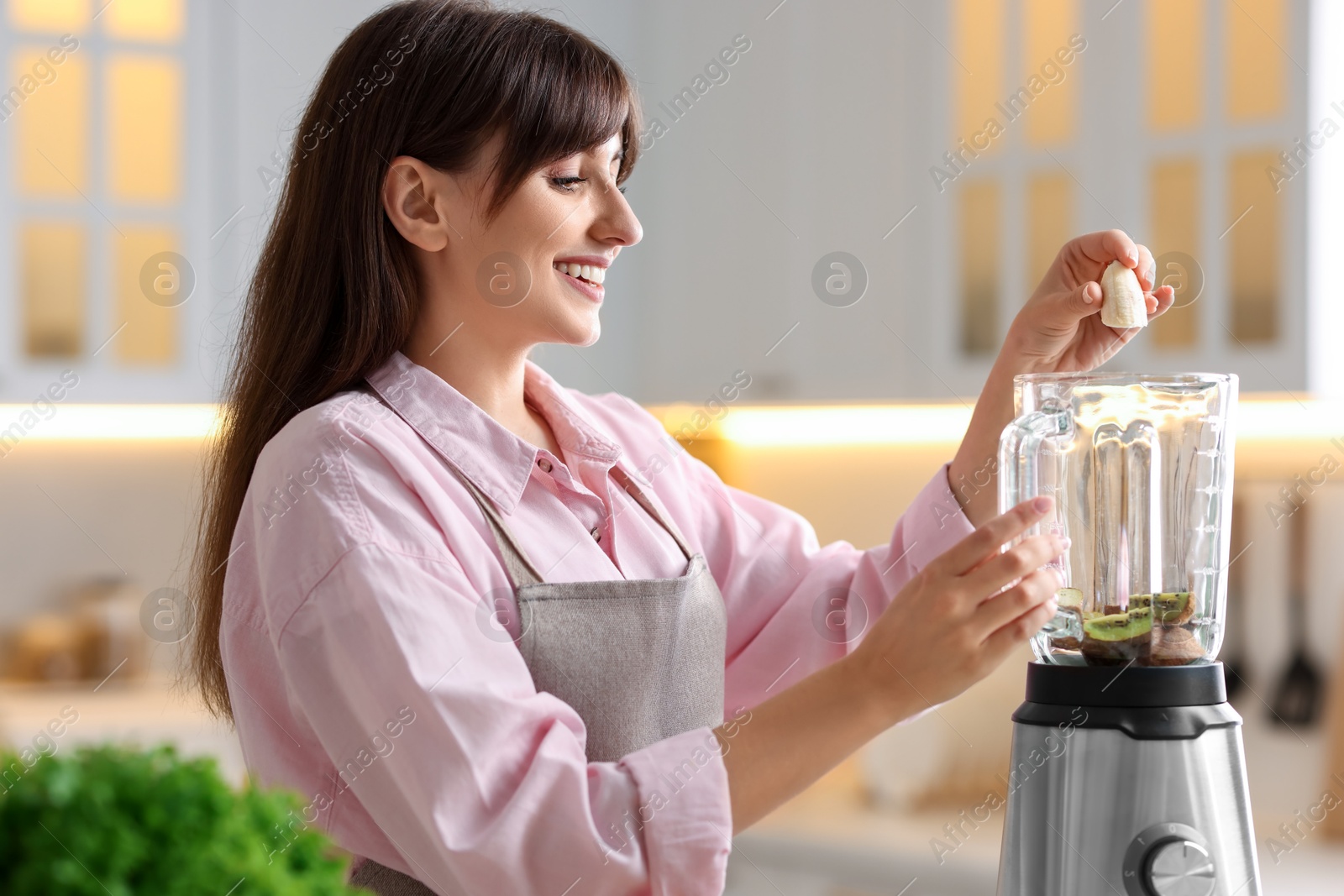 Photo of Young woman making delicious smoothie with blender in kitchen