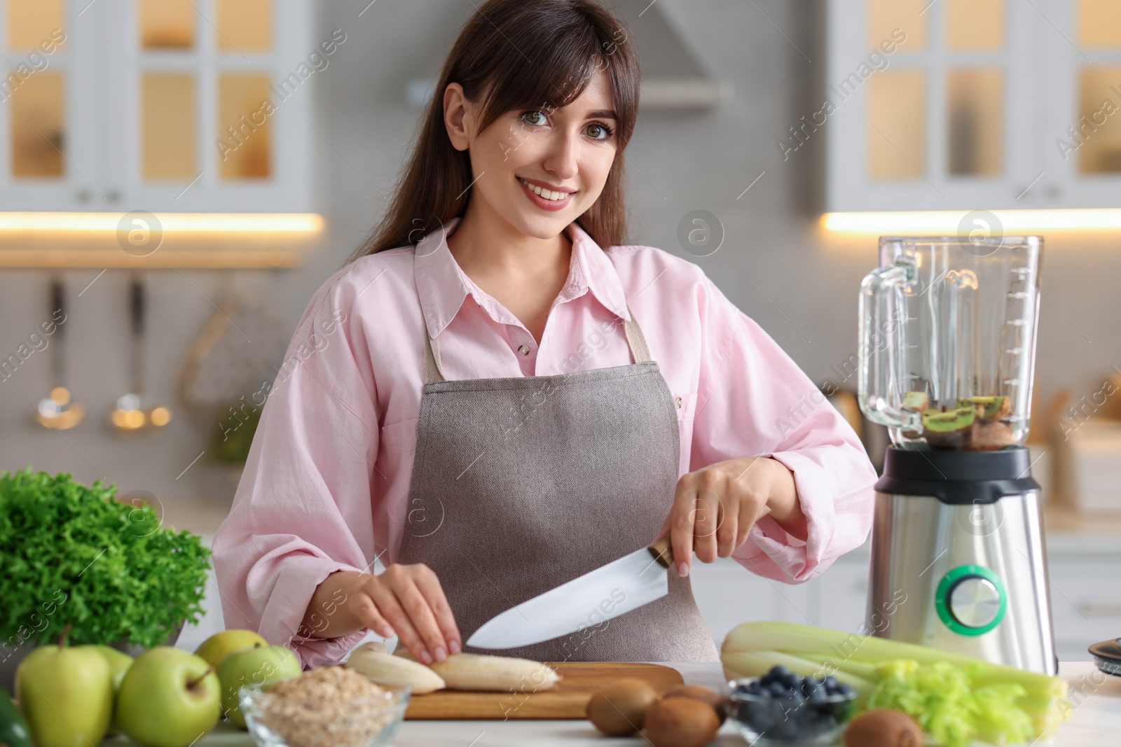 Photo of Young woman making delicious smoothie with blender at white marble table in kitchen