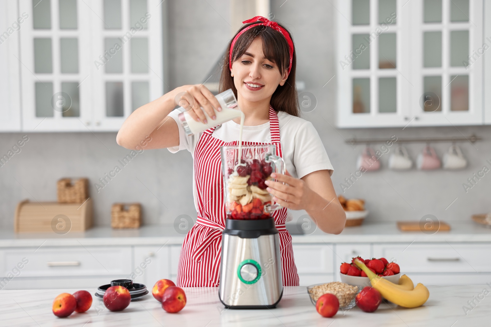 Photo of Young woman making delicious smoothie with blender at white marble table in kitchen