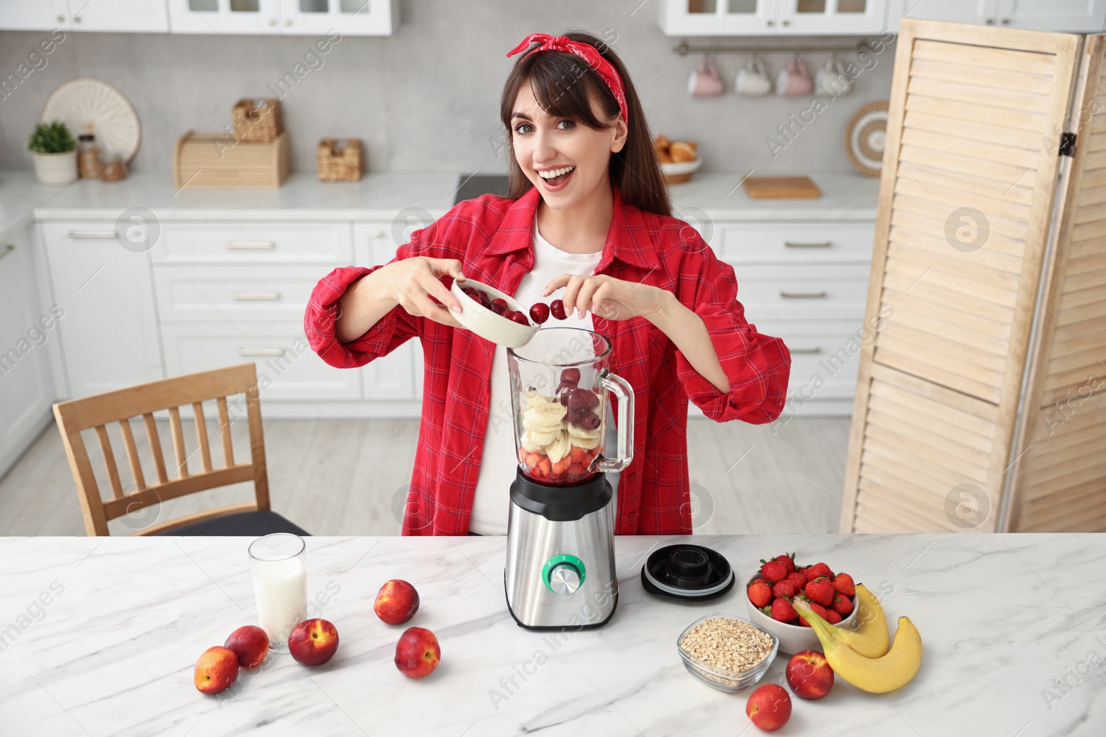 Photo of Young woman making delicious smoothie with blender at white marble table in kitchen