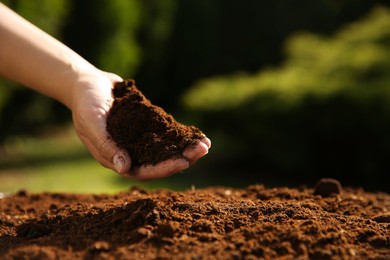 Woman holding pile of soil outdoors, closeup. Space for text