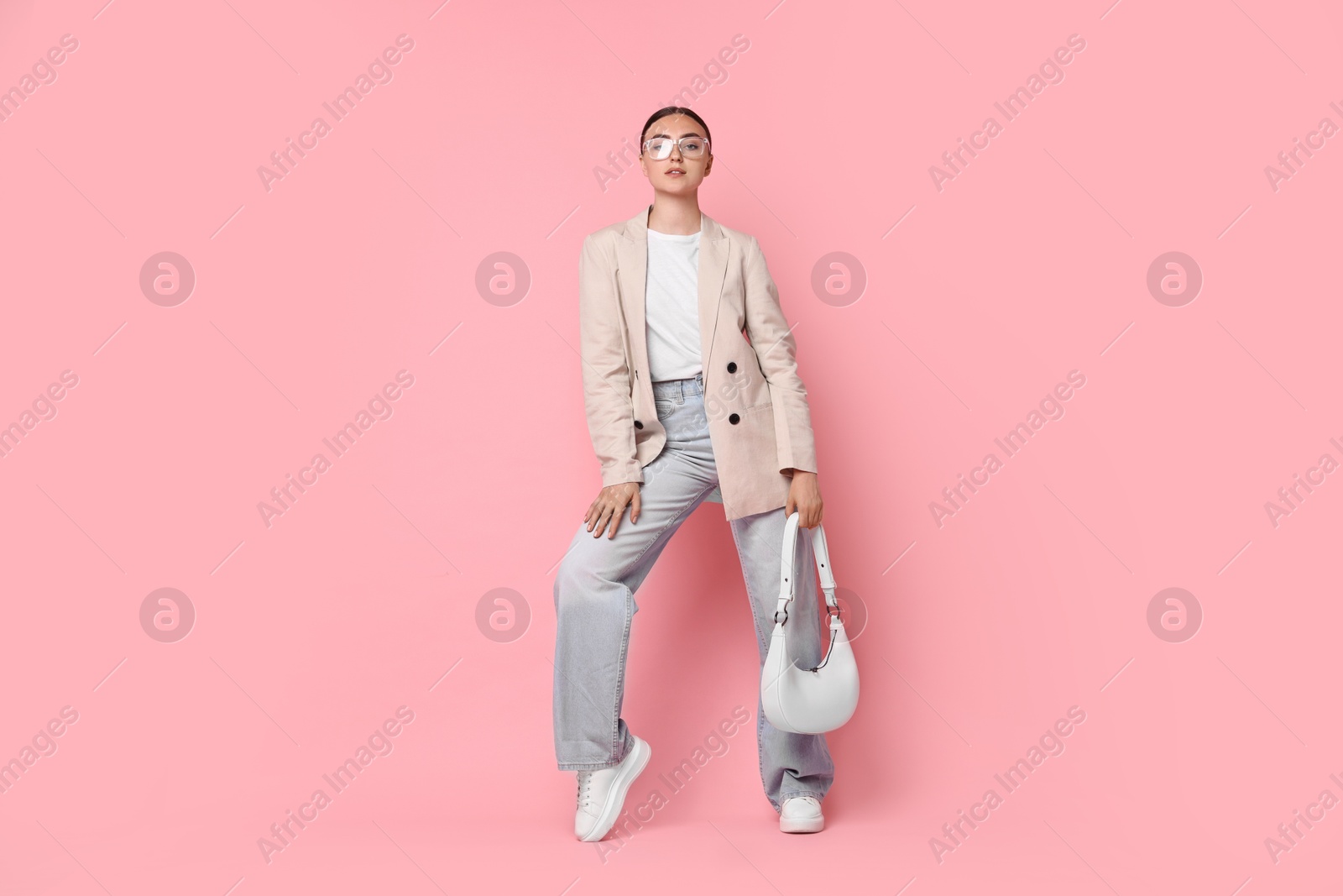 Photo of Stylish woman in beige jacket with bag on pink background