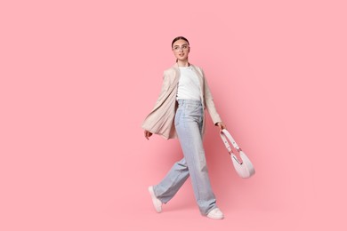 Photo of Stylish woman in beige jacket with bag walking on pink background