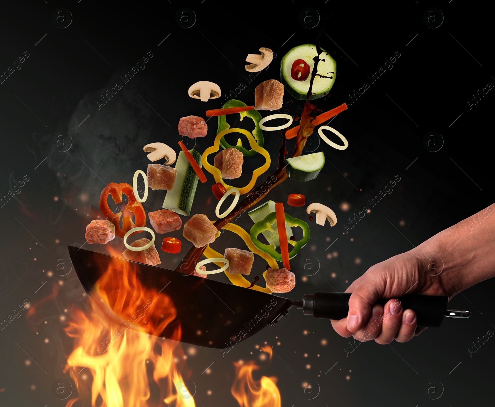 Image of Man tossing ingredients in wok over fire on black background, closeup