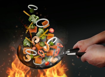 Image of Man tossing ingredients in wok over fire on black background, closeup