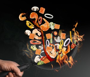 Image of Man tossing ingredients in wok over fire on black background, closeup