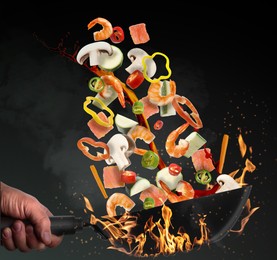 Image of Man tossing ingredients in wok over fire on black background, closeup