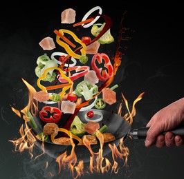 Man tossing ingredients in wok over fire on black background, closeup