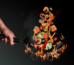 Image of Man tossing ingredients in wok over fire on black background, closeup