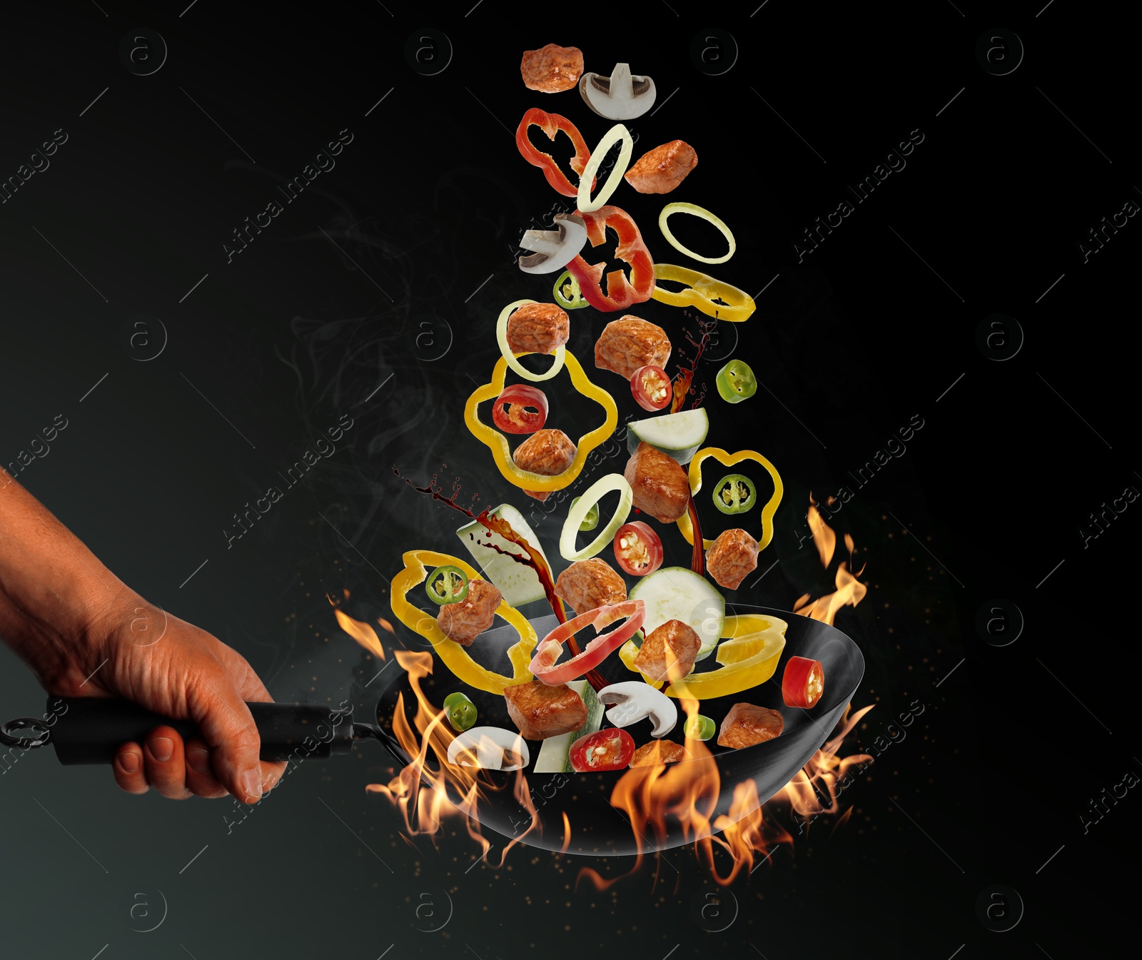 Image of Man tossing ingredients in wok over fire on black background, closeup